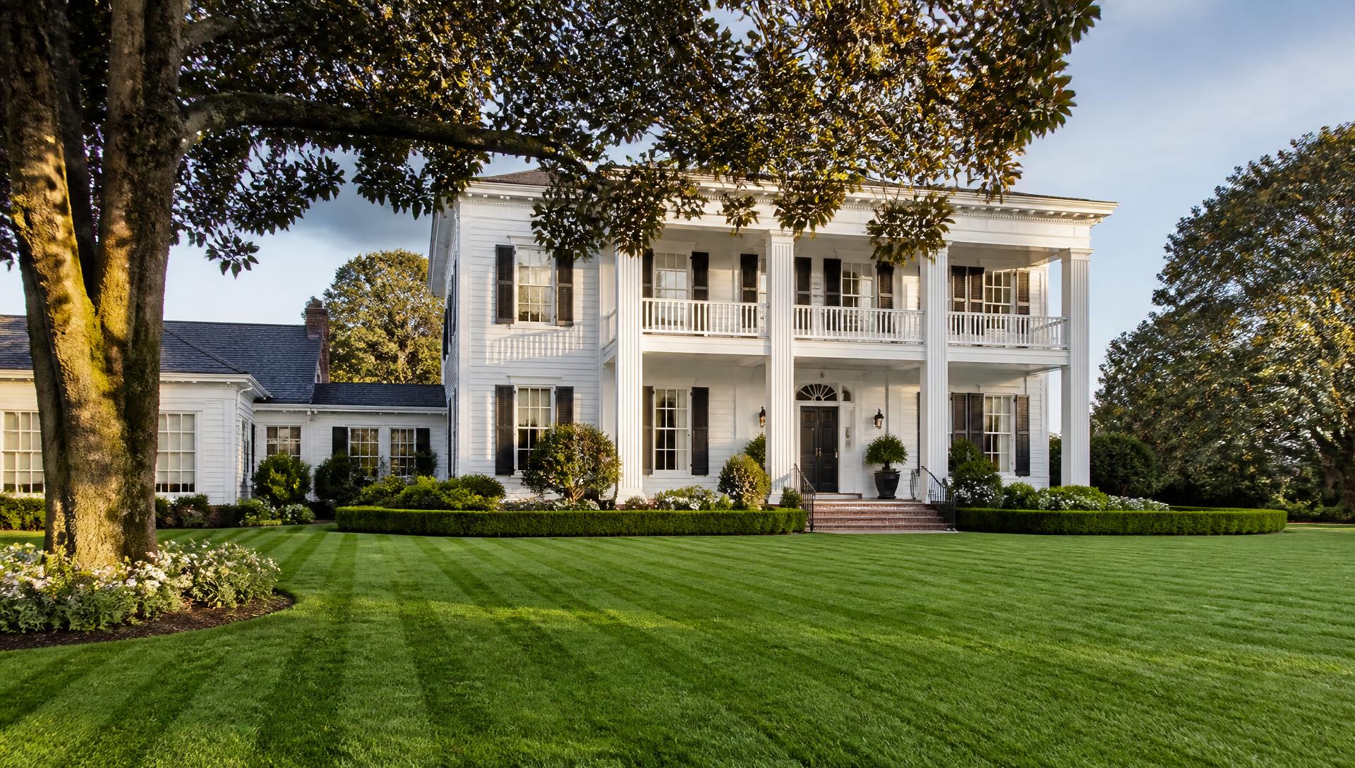 A white Southern colonial home behind a freshly striped, deep-green lawn